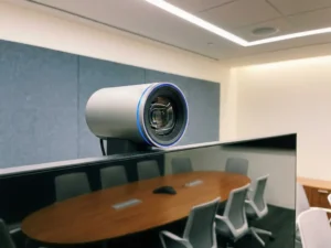 AI-conferentiecamera op moderne monitor in zakelijke vergaderruimte, met ovale tafel op de achtergrond.