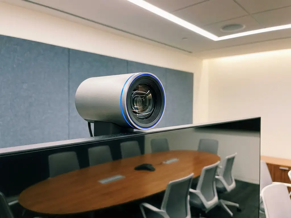 AI-conferentiecamera op moderne monitor in zakelijke vergaderruimte, met ovale tafel op de achtergrond.