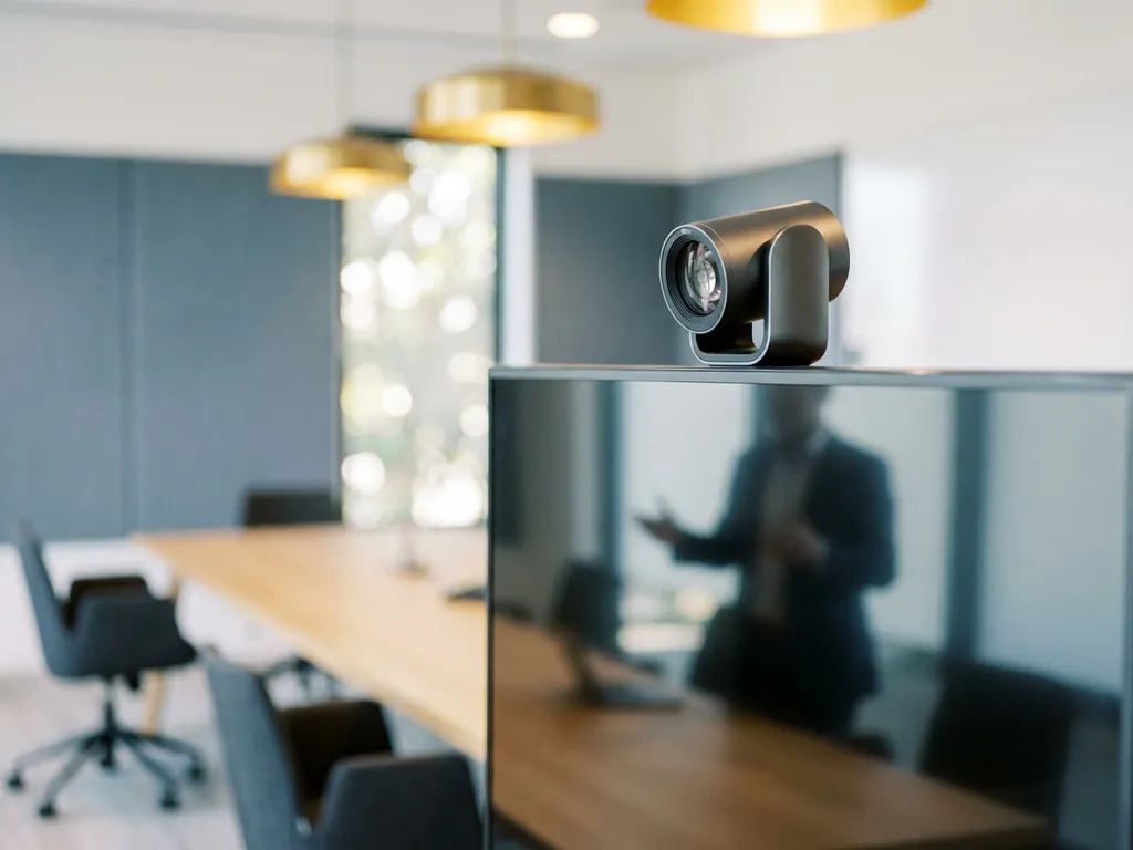 Auto-tracking vergadercamera op monitor gericht op professional in moderne boardroom met lange tafel en warme verlichting.