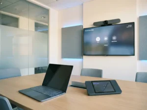 Laptop en Microsoft Teams Rooms-console met groothoeklens op een moderne vergadertafel in kantooromgeving.