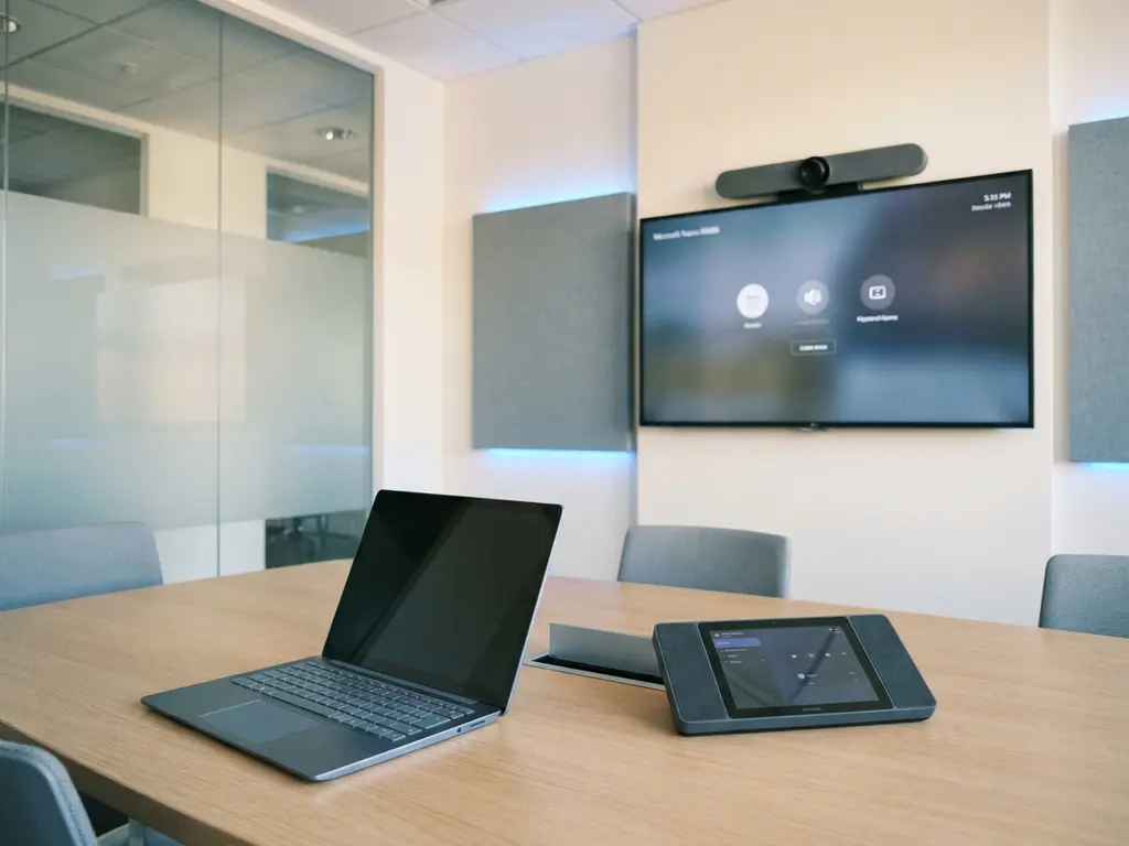 Laptop en Microsoft Teams Rooms-console met groothoeklens op een moderne vergadertafel in kantooromgeving.