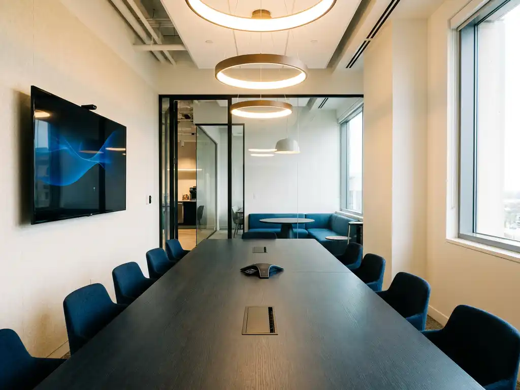 Moderne vergaderruimte met grote boardroomtafel, AV-scherm en glazen wand naar huddle space, warm licht en blauwe accenten.