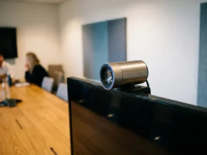 Conferentiecamera op een scherm met blauwe lensreflectie, vergadertafel met houten oppervlak op de achtergrond.